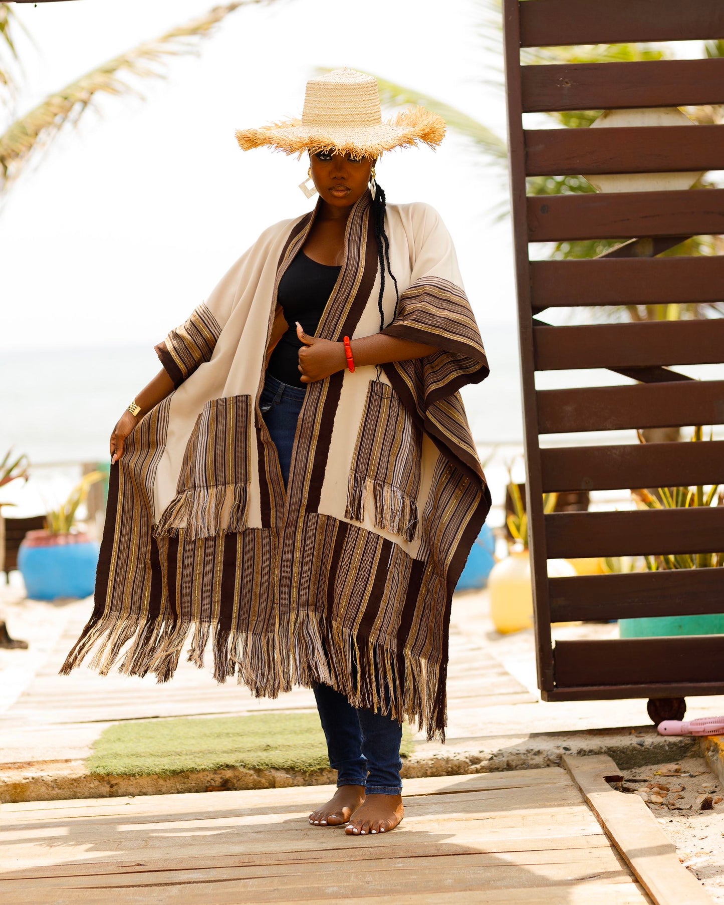 This standout piece is crafted from a thick black cotton crepe base, elevated with boldly striped multicolored woven Asooke panels that trim the silhouette. The edges are intentionally frayed—yet securely finished—creating a striking tassel effect that adds texture and movement to the hem. Complete with matching frayed Asooke patch pockets, this jacket is a cultural classic reimagined for the contemporary wardrobe.