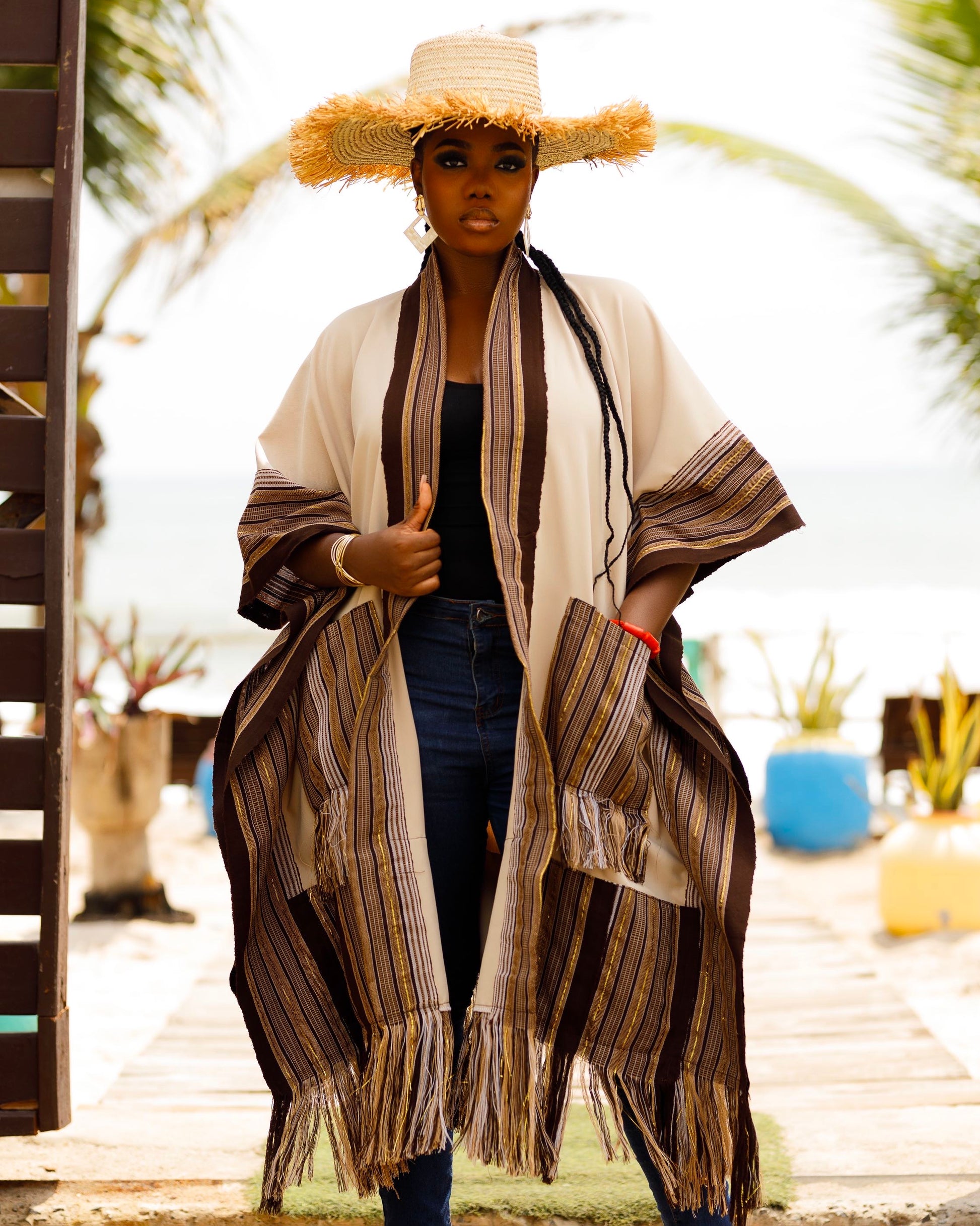 This standout piece is crafted from a thick black cotton crepe base, elevated with boldly striped multicolored woven Asooke panels that trim the silhouette. The edges are intentionally frayed—yet securely finished—creating a striking tassel effect that adds texture and movement to the hem. Complete with matching frayed Asooke patch pockets, this jacket is a cultural classic reimagined for the contemporary wardrobe.