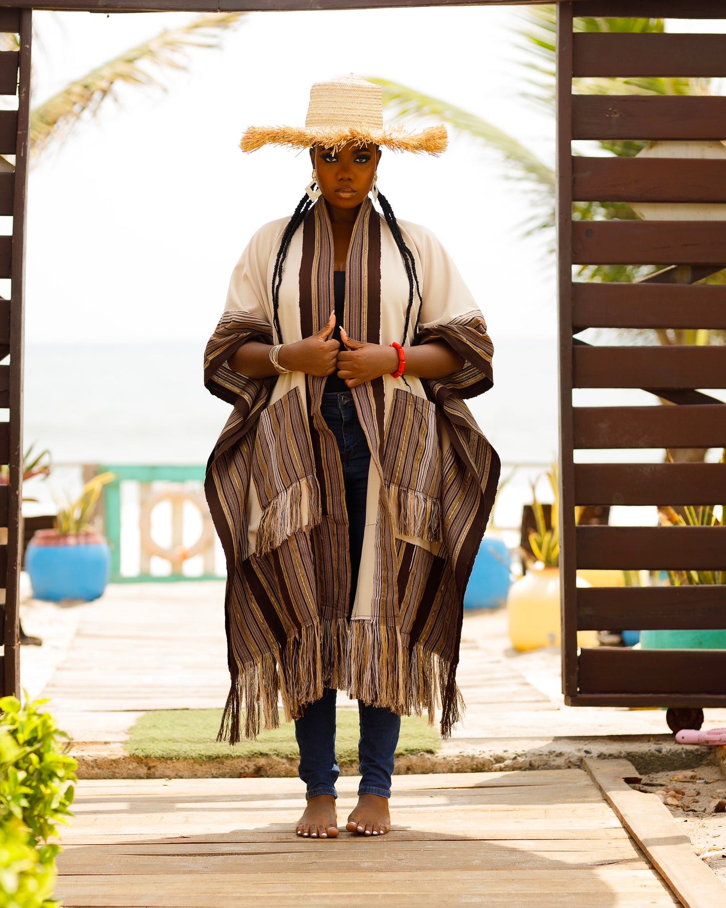 This standout piece is crafted from a thick black cotton crepe base, elevated with boldly striped multicolored woven Asooke panels that trim the silhouette. The edges are intentionally frayed—yet securely finished—creating a striking tassel effect that adds texture and movement to the hem. Complete with matching frayed Asooke patch pockets, this jacket is a cultural classic reimagined for the contemporary wardrobe.
