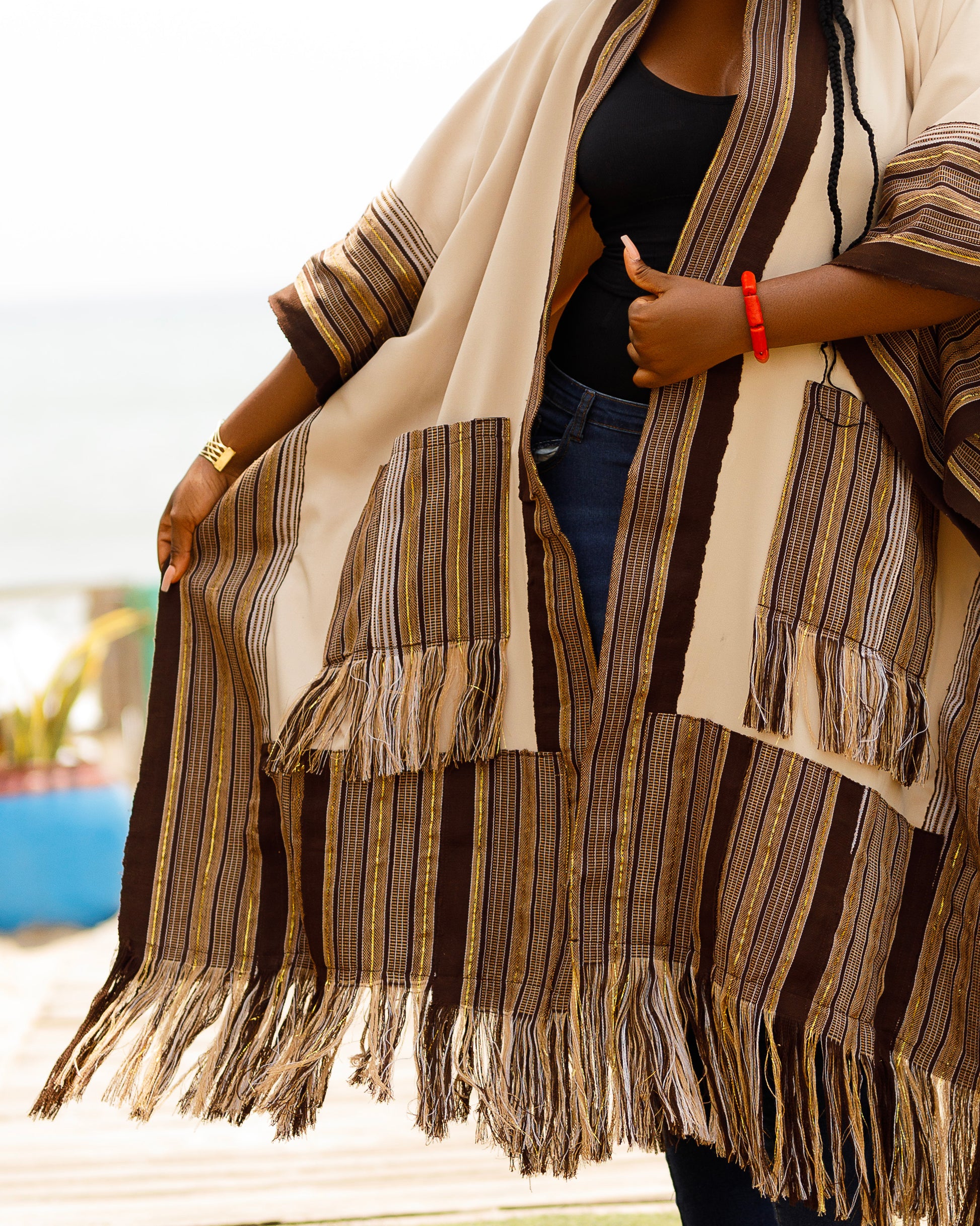 This standout piece is crafted from a thick black cotton crepe base, elevated with boldly striped multicolored woven Asooke panels that trim the silhouette. The edges are intentionally frayed—yet securely finished—creating a striking tassel effect that adds texture and movement to the hem. Complete with matching frayed Asooke patch pockets, this jacket is a cultural classic reimagined for the contemporary wardrobe.