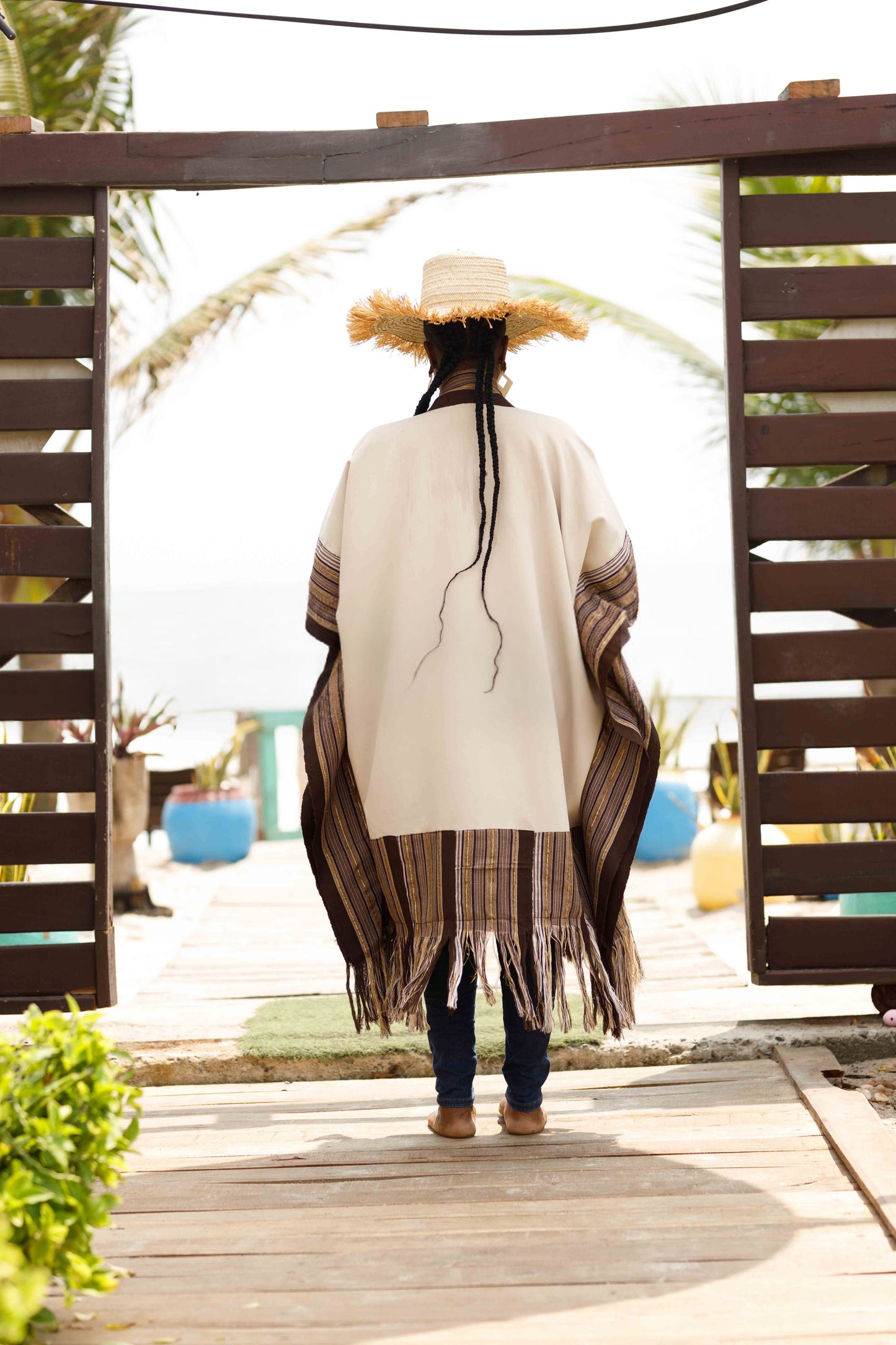 This standout piece is crafted from a thick black cotton crepe base, elevated with boldly striped multicolored woven Asooke panels that trim the silhouette. The edges are intentionally frayed—yet securely finished—creating a striking tassel effect that adds texture and movement to the hem. Complete with matching frayed Asooke patch pockets, this jacket is a cultural classic reimagined for the contemporary wardrobe.