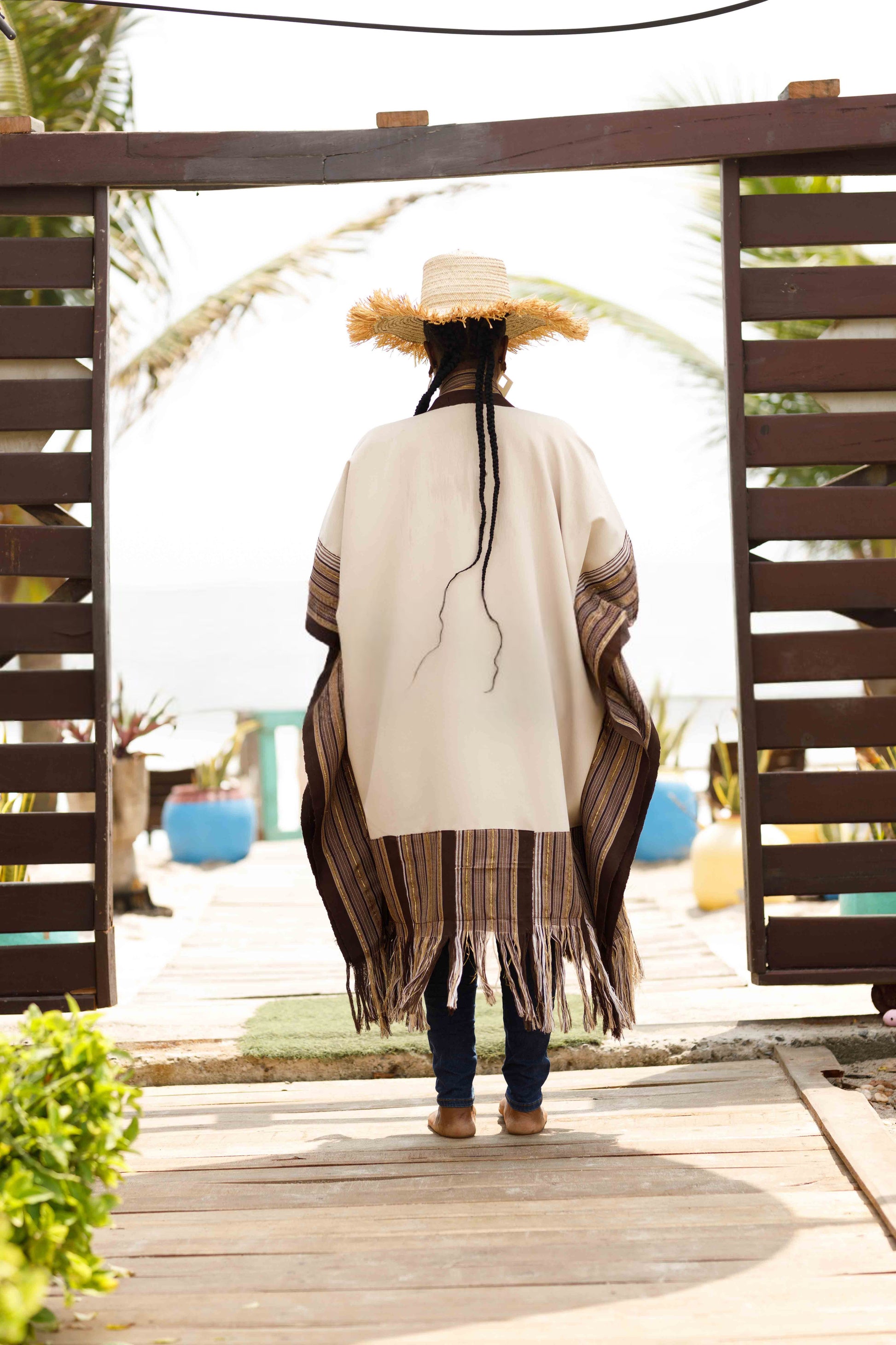 This standout piece is crafted from a thick black cotton crepe base, elevated with boldly striped multicolored woven Asooke panels that trim the silhouette. The edges are intentionally frayed—yet securely finished—creating a striking tassel effect that adds texture and movement to the hem. Complete with matching frayed Asooke patch pockets, this jacket is a cultural classic reimagined for the contemporary wardrobe.