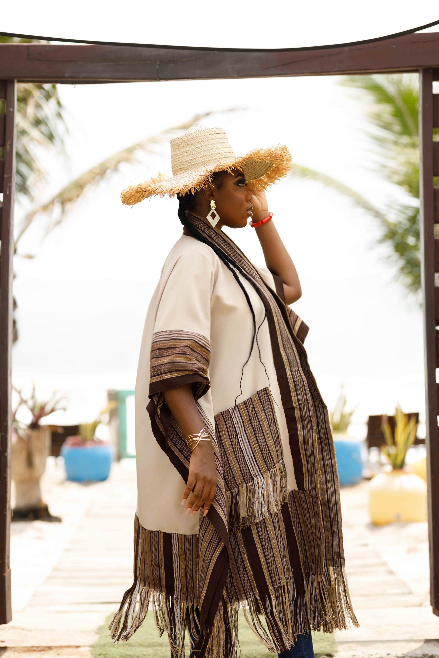 This standout piece is crafted from a thick black cotton crepe base, elevated with boldly striped multicolored woven Asooke panels that trim the silhouette. The edges are intentionally frayed—yet securely finished—creating a striking tassel effect that adds texture and movement to the hem. Complete with matching frayed Asooke patch pockets, this jacket is a cultural classic reimagined for the contemporary wardrobe.