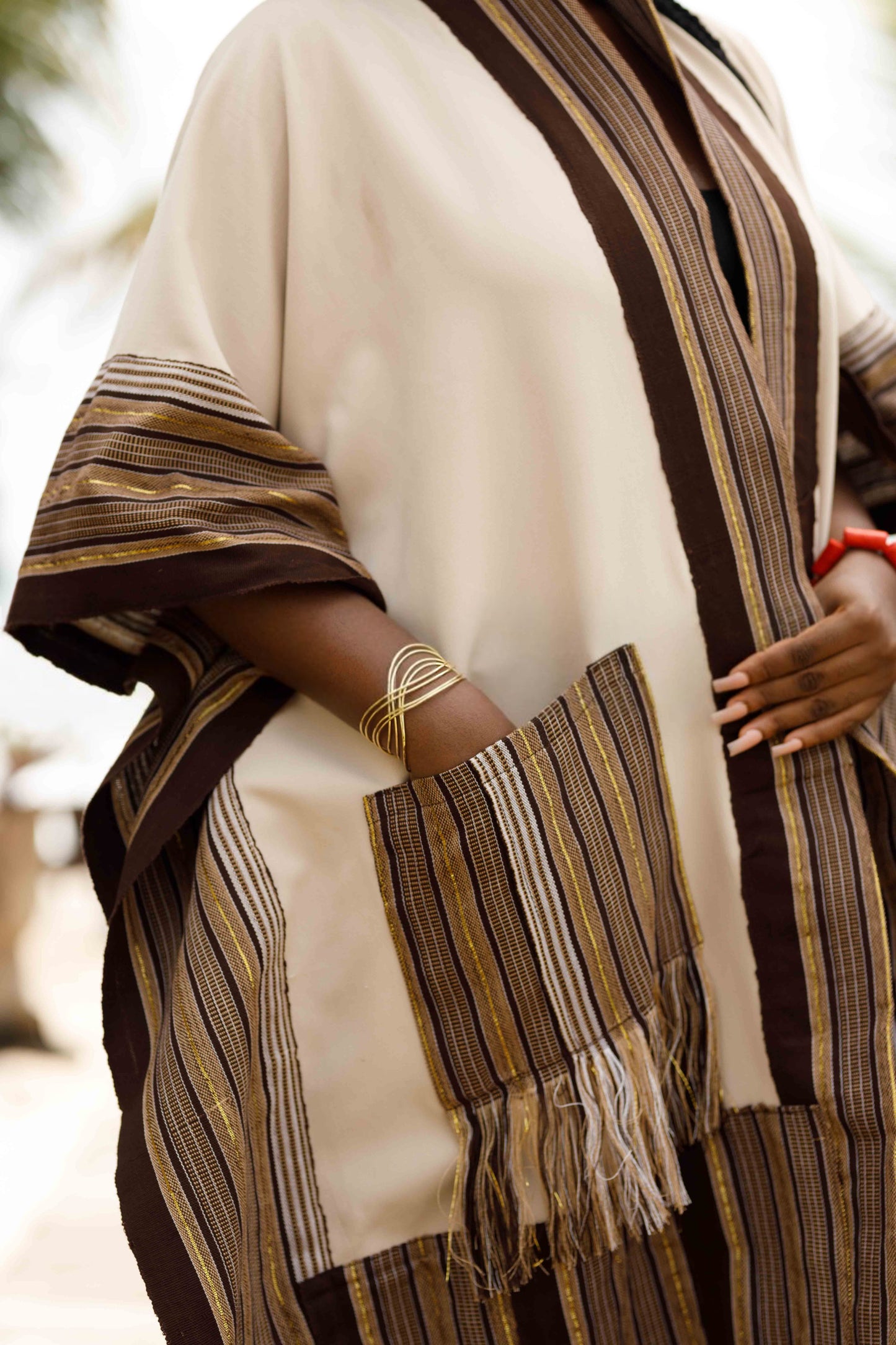 This standout piece is crafted from a thick black cotton crepe base, elevated with boldly striped multicolored woven Asooke panels that trim the silhouette. The edges are intentionally frayed—yet securely finished—creating a striking tassel effect that adds texture and movement to the hem. Complete with matching frayed Asooke patch pockets, this jacket is a cultural classic reimagined for the contemporary wardrobe.