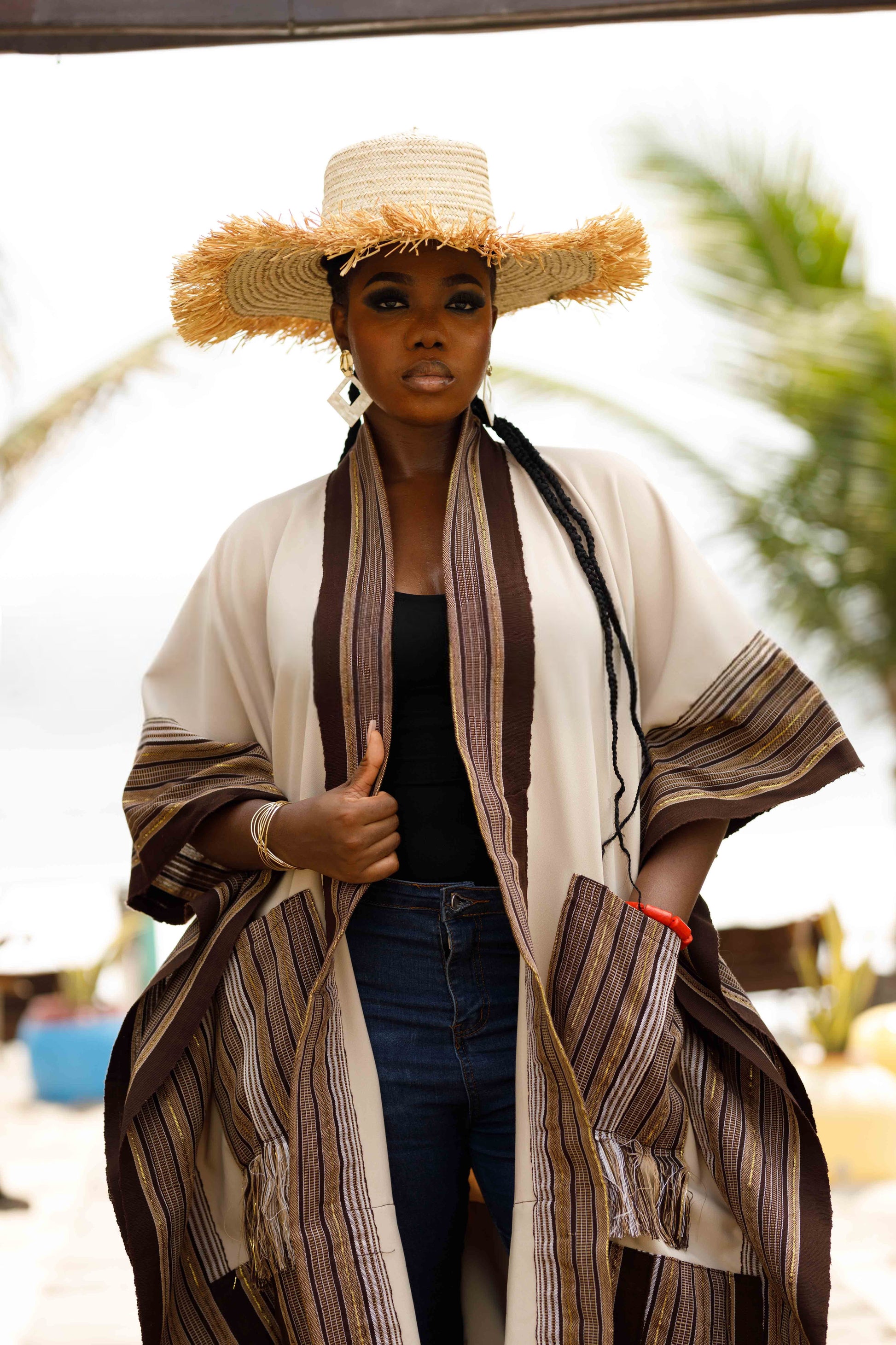 This standout piece is crafted from a thick black cotton crepe base, elevated with boldly striped multicolored woven Asooke panels that trim the silhouette. The edges are intentionally frayed—yet securely finished—creating a striking tassel effect that adds texture and movement to the hem. Complete with matching frayed Asooke patch pockets, this jacket is a cultural classic reimagined for the contemporary wardrobe.
